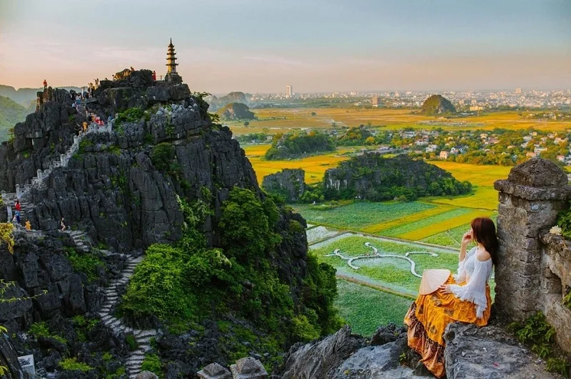Ninh Binh 3 Day Itinerary: The Perfect Guide to Nature, Culture and Hidden Gems An adventurous traveler standing beside the iconic dragon shrine on the peak of Mua Cave at golden hour.