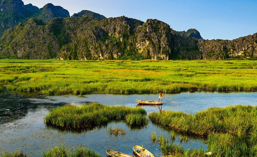 Ninh Binh 3 Day Itinerary: The Perfect Guide to Nature, Culture and Hidden Gems A quiet bamboo boat gliding through open lagoons and tall reeds at Van Long Nature Reserve.